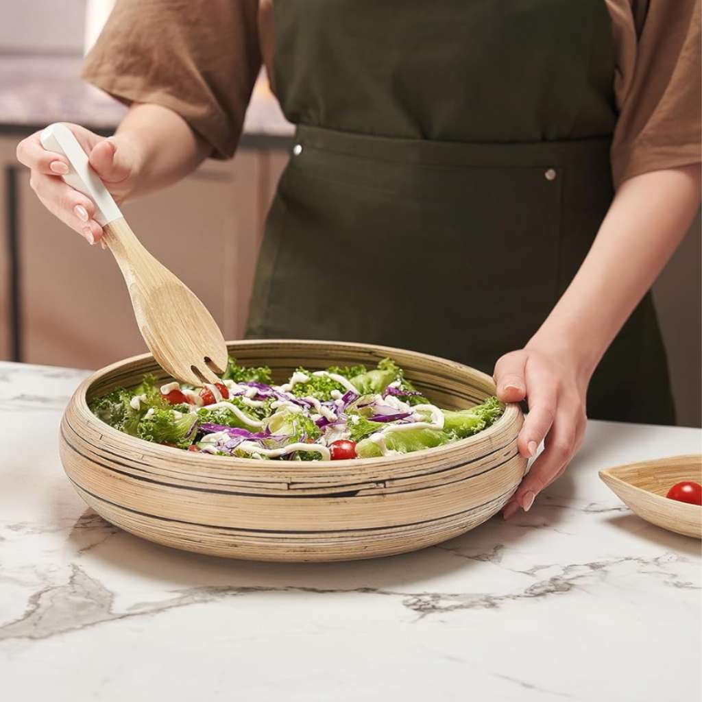 Sustainable natural bamboo bowl filled with healthy green salad, being served with wooden spoon and fork in modern kitchen setting
